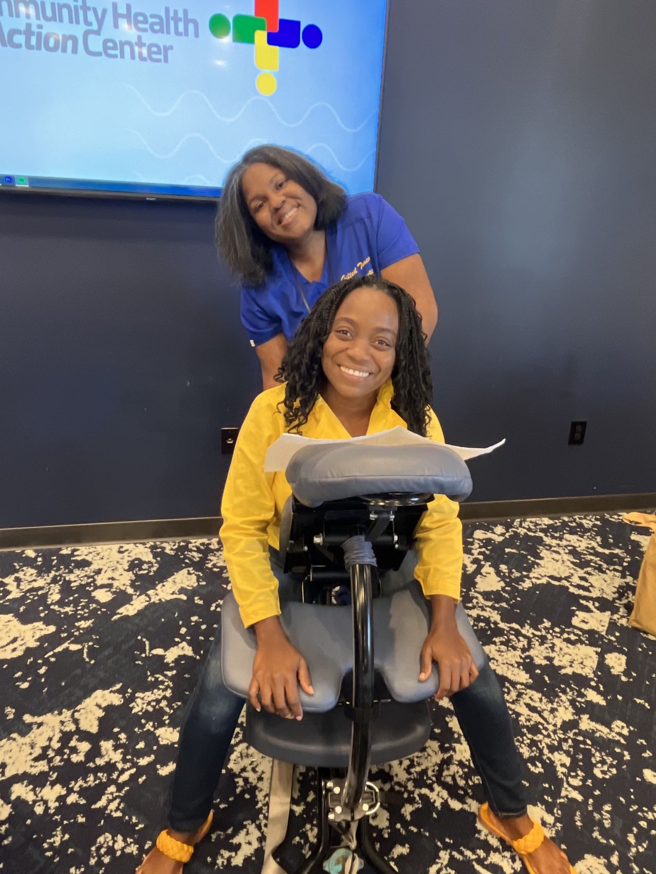 Etete giving a seated chair massage to a smiling client at a Huntsville community health event