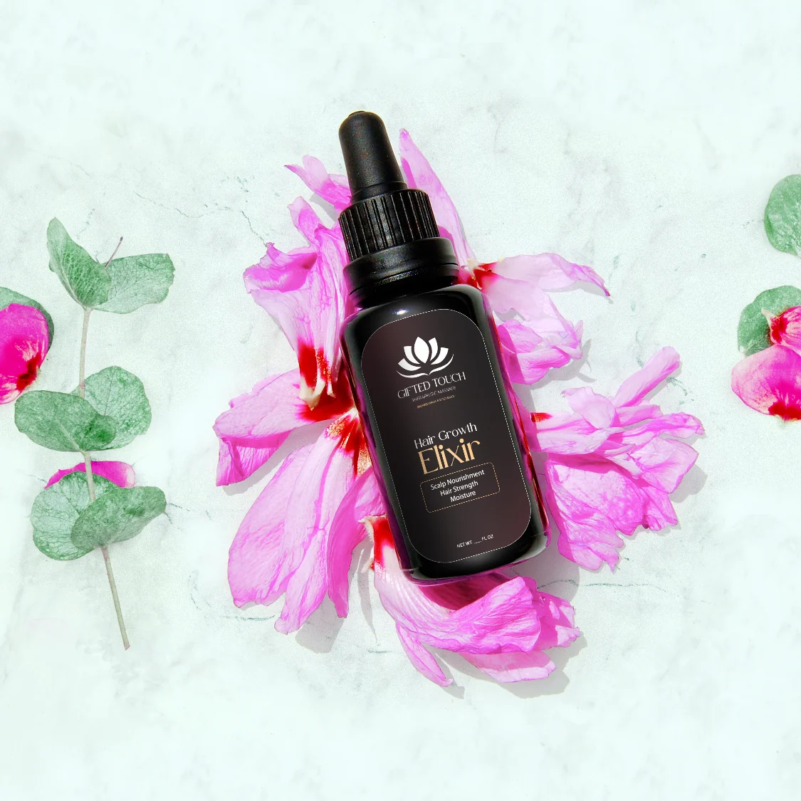 Hair Growth Elixir in its new Gifted Touch label, styled on marble with pink flowers